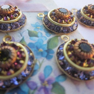 May include: Five gold-toned metal charms with a layered design. Each charm features a central black gemstone surrounded by smaller purple gemstones and a gold-toned rim.