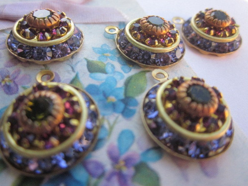 May include: Five gold-toned metal charms with a layered design. Each charm features a central black gemstone surrounded by smaller purple gemstones and a gold-toned rim.