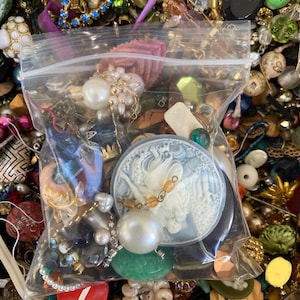 May include: A clear plastic bag filled with a variety of colorful beads, buttons, and other craft supplies. The bag is sitting on a surface covered in a variety of other craft supplies.