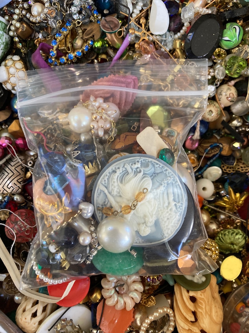 May include: A clear plastic bag filled with a variety of colorful beads, buttons, and other craft supplies. The bag is sitting on a surface covered in a variety of other craft supplies.