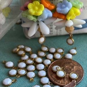 May include: A large quantity of small, white, faceted glass beads with gold-toned metal loops. The beads are scattered on a teal surface, with a few beads on a copper-colored coin.