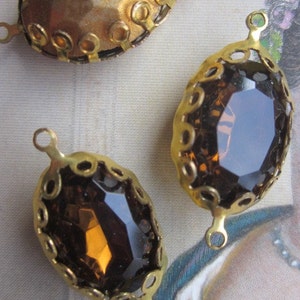 Pode incluir: Tr&ecirc;s engastes de metal dourado com pedras de vidro ovais. As pedras s&atilde;o transparentes com um tom castanho. Os engastes t&ecirc;m uma borda decorativa de pequenos c&iacute;rculos.