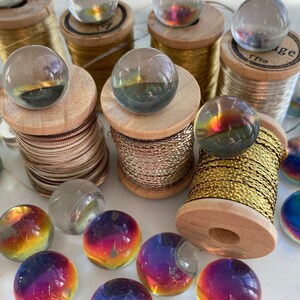 Peut inclure: Une collection de billes en verre iris&eacute;es et de billes en verre transparent sur des bobines de fil d'or et d'argent. Les billes sont dispos&eacute;es en cercle autour des bobines.