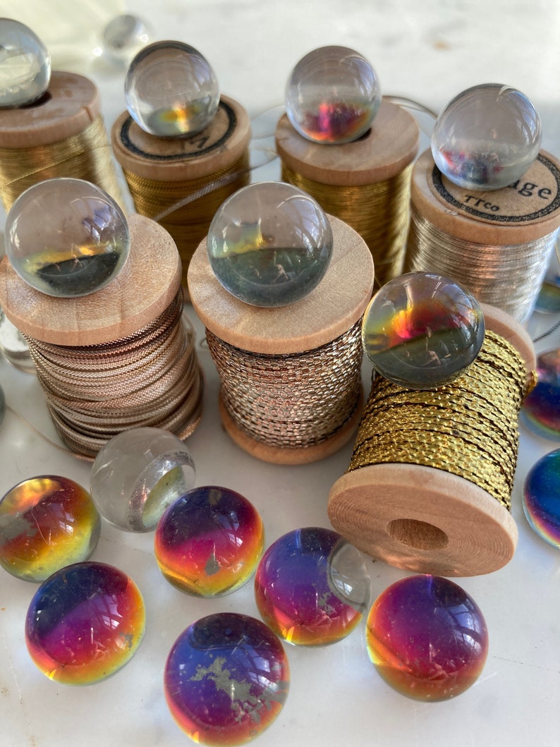 Peut inclure: Une collection de billes en verre iris&eacute;es et de billes en verre transparent sur des bobines de fil d'or et d'argent. Les billes sont dispos&eacute;es en cercle autour des bobines.