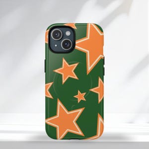 Op de afbeelding: Een groene telefoonhoes met een patroon van oranje sterren. De hoes heeft een zwarte rand en een uitsparing voor de camera. De sterren zijn wit omlijnd en variëren in grootte.