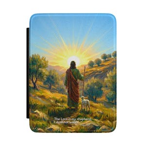 May include: A rectangular protective tablet case featuring a printed landscape illustration of a figure in a robe holding a staff with a small lamb in a grassy field at sunrise. The text reads: The Lord is my shepherd; I shall not want. Psalm 23:1.