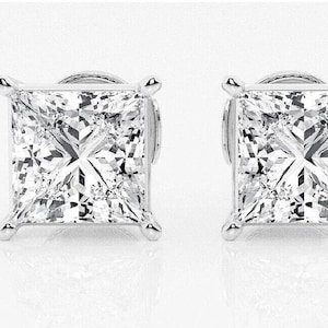 May include: A pair of square-cut diamond stud earrings. Each earring features a large, clear, and faceted diamond set in a silver or white gold setting. The earrings are displayed against a white background.