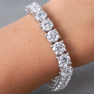 Peut inclure: Un bracelet tennis argenté composé d'une rangée continue de pierres rondes, transparentes et facettées, fixées dans des montures métalliques à quatre griffes. Le bracelet entoure le poignet, mettant en valeur la brillance des pierres.