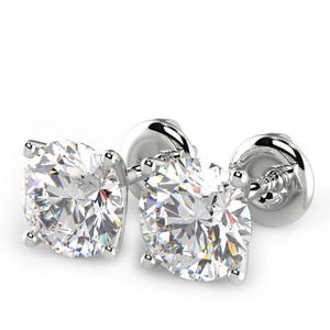 May include: A pair of round-cut stud earrings featuring clear, faceted stones set in four-prong silver-toned metal settings. Each earring includes a secure screw-back post mechanism, showcasing a brilliant, reflective surface and a classic design.