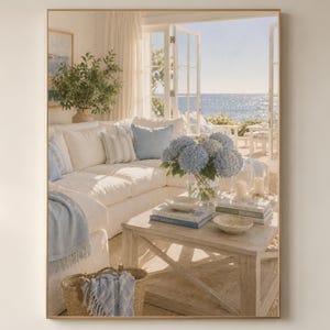 Pode incluir: Impressão emoldurada de uma sala de estar clara com vista para o mar. Um sofá branco é adornado com almofadas azuis e brancas e uma manta azul. Uma mesa de centro de madeira exibe livros, velas e uma tigela, com um vaso de hortênsias azuis.