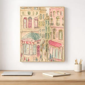 Framed Parisian watercolor print styled on a white desk beside a laptop and minimal stationery in a bright home office