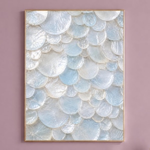 Könnte beinhalten: Ein rechteckiges Wandkunstwerk mit einem geschichteten, überlappenden Muster aus kreisförmigen, irisierenden weißen und hellblauen muschelartigen Scheiben. Das Kunstwerk ist in einen dünnen, goldfarbenen Metallrahmen gefasst und erzeugt eine texturierte, reflektierende Oberfläche.