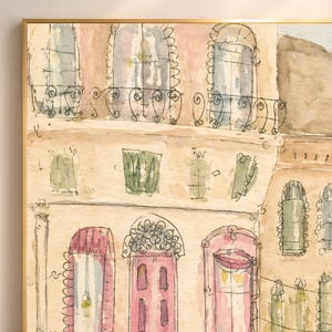 Close-up detail of Parisian watercolor wall art showing ornate pink doors, green shutters, and warm cream building facades