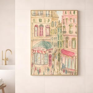 Parisian watercolor art print in a wood frame leaning against a white bathroom wall beside a gold faucet and minimal decor