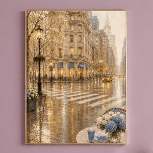May include: A vertical wall art print depicting a rainy New York City street scene with a corner building, a yellow taxi, and a crosswalk. In the foreground, a round table holds a vase of blue and white hydrangeas, a blue cup, and a book.