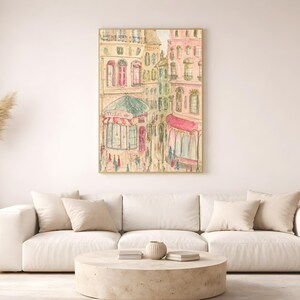 Parisian street scene print in a thin wood frame hung on a white wall above a neutral linen sofa with dried pampas grass