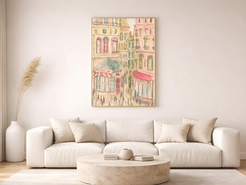 Parisian street scene print in a thin wood frame hung on a white wall above a neutral linen sofa with dried pampas grass