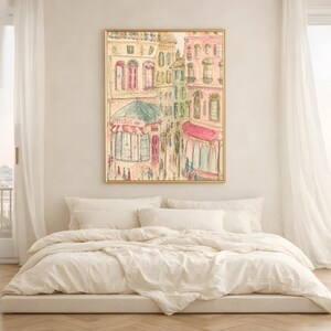 Parisian street scene wall art in a warm wood frame above a white bedside table with soft natural bedding and curtains