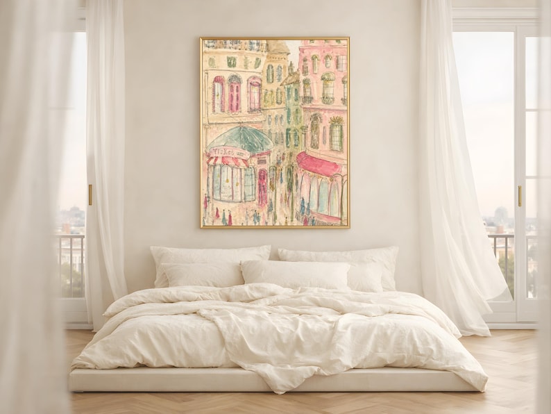 Parisian street scene wall art in a warm wood frame above a white bedside table with soft natural bedding and curtains