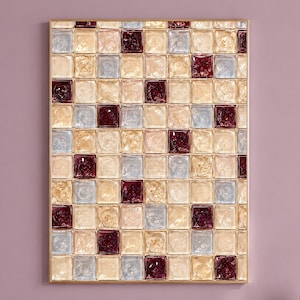 May include: A rectangular wall art piece featuring a grid of square tiles in shades of deep burgundy, pale blue, and shimmering gold. The tiles have a textured, glossy finish and are arranged in a repeating pattern within a thin gold frame.