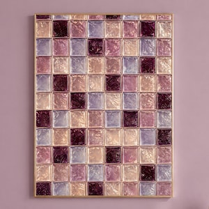 May include: A rectangular wall art piece featuring a grid of square glass tiles in shades of deep plum, soft lavender, and pale peach. Each tile has a textured, rippled surface that catches the light, all encased within a thin, metallic gold frame.