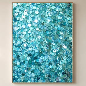 May include: A framed artwork featuring a dense pattern of turquoise and teal sequins. The circular sequins are arranged closely together, creating a shimmering, textured surface. The artwork is encased in a simple, light-colored wooden frame.