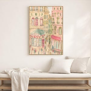 Parisian street scene print in a light wood frame displayed on a white wall beside a neutral linen bed