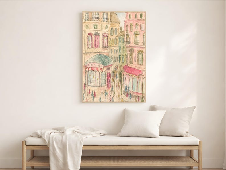Parisian street scene print in a light wood frame displayed on a white wall beside a neutral linen bed