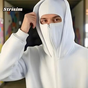 Könnte beinhalten: Ein weißer Kapuzenpullover mit Vollgesichtsbedeckung. Der Pullover hat einen Reißverschluss vorne und der Markenname "Strisim" ist in der oberen linken Ecke sichtbar. Die Person trägt die Kapuze und die Gesichtsbedeckung.