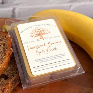 May include: A clear plastic container holding a Farmstand Banana Nut Bread scented soy wax melt. The label features text and a tree graphic. A ripe banana and a slice of banana bread are in the background. The wax melt weighs 2.7 oz (76 g).