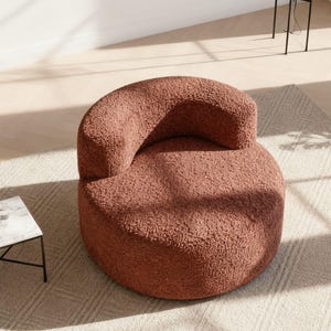 May include: A round, terracotta-colored armchair with a curved back and armrest. The chair sits on a light-colored rug. A small, square side table with a marble top and black legs is next to the chair. A floor lamp with a glass globe is in the background.