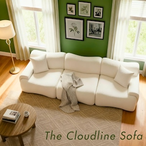 May include: A large, off-white sectional sofa with a rounded design, accompanied by white throw pillows and a light gray blanket. A round wooden coffee table and a gold floor lamp are in the foreground. The text "The Cloudline Sofa" is at the bottom.