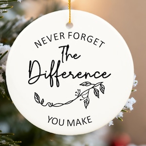 Peut inclure: Ornement de Noël rond en céramique blanche avec l'inscription noire "NEVER FORGET The Difference YOU MAKE". Une ficelle dorée est attachée pour l'accrocher. Décoré d'un motif floral.