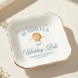 Może przedstawiać: Biały ceramiczny talerz ze złotą obwódką, z napisem "Seashells and Wedding Bells" i ilustracją muszli. Talerz zawiera rok "2025" oraz imiona "Harrison & Michaela, Charleston, SC."