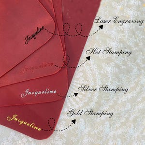 May include: A close-up of red leather samples with the name "Jacqueline" displayed using different techniques: laser engraving, hot stamping, silver stamping, and gold stamping. The samples are arranged to showcase the various methods.