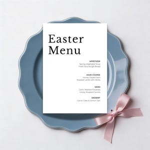 Può includere: Un piatto azzurro con bordo smerlato mostra un biglietto del menu bianco con le parole "Easter Menu" in nero. Il menu elenca i piatti. Un fiocco di nastro rosa è a destra. Il piatto misura circa 25 cm di diametro.