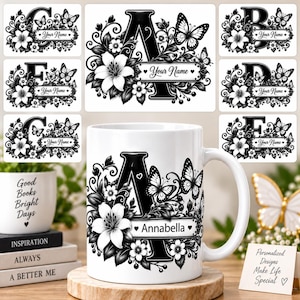 May include: A white ceramic mug featuring a black letter A surrounded by floral patterns and butterflies, with the name Annabella printed on a rectangular label. The design includes lilies and vines, matching the alphabet labels shown above.