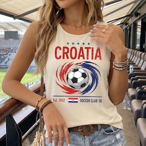 May include: A cream-colored sleeveless tank top featuring the word CROATIA in red, five blue stars, and a central graphic of a soccer ball surrounded by red and blue swirls. Below, the text reads Est. 1912, a small Croatian flag, and SOCCER CLUB '26.