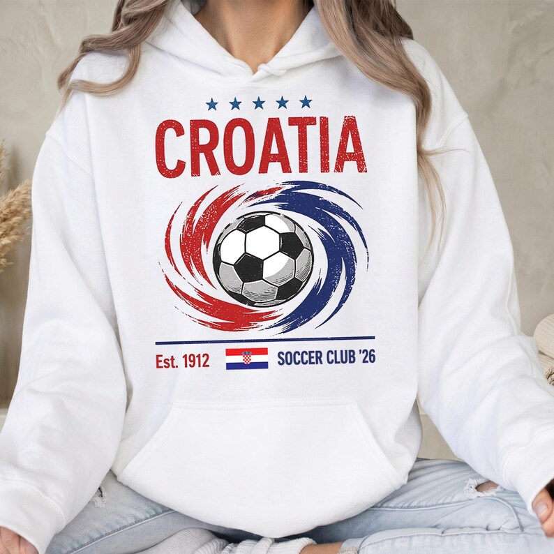 K&ouml;nnte beinhalten: Ein wei&szlig;er Kapuzenpullover mit einer Grafik, die den roten Schriftzug CROATIA, f&uuml;nf blaue Sterne, einen schwarz-wei&szlig;en Fu&szlig;ball umgeben von roten und blauen Wirbeln sowie den Text Est. 1912, eine kroatische Flagge und SOCCER CLUB '26 zeigt.