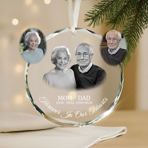 Può includere: Un ornamento di cristallo trasparente e sfaccettato con tre foto incastonate di una coppia di anziani. L'ornamento riporta le parole "Mom Dad Forever In Our Hearts" e gli anni 1950-2025 e 1949-2022. Un nastro bianco è attaccato per appenderlo.