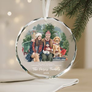 Può includere: Una palla di Natale in vetro trasparente e sfaccettato con un ritratto di famiglia all'interno. L'immagine mostra una famiglia con un cane in un camion, con il testo "The Perez Family 2025". Un nastro bianco è attaccato per appenderla.