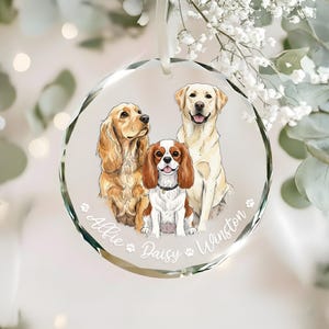 Op de afbeelding: Een heldere, ronde glazen ornament met illustraties van drie honden: een Cocker Spaniel, een Cavalier King Charles Spaniel en een Labrador Retriever. De namen "Allie", "Daisy" en "Winston" staan op de rand.