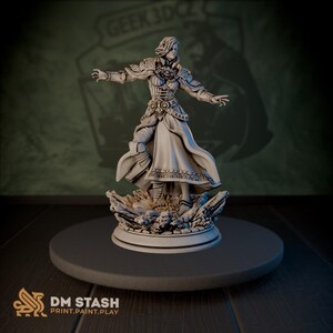 Op de afbeelding: Een gedetailleerd, wit 3D-geprint beeldje van een vrouw in versierd harnas en vloeiende gewaden, met uitgestrekte armen. Het beeldje staat op een rotsachtige basis. Het DM STASH-logo is onderaan zichtbaar.