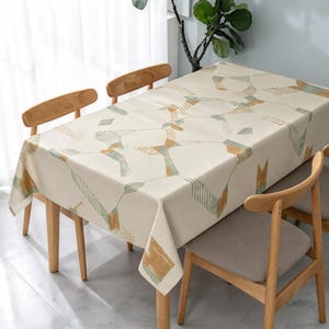 May include: A rectangular tablecloth with an off-white base color featuring a geometric pattern of interconnected lines and shapes in muted sage green and mustard yellow, with some sections displaying a fine striped texture.