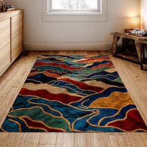 May include: A rectangular area rug with a colorful, abstract design. The rug features a pattern of flowing lines and shapes in shades of blue, red, gold, and green. The rug is placed on a wooden floor in a room with natural light.