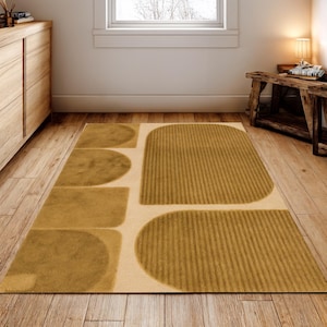 Könnte beinhalten: Ein rechteckiger Teppich mit einem geometrischen Design in Beige- und Senfgelbtönen. Der Teppich hat abgerundete und rechteckige Formen mit einem strukturierten, gestreiften Muster auf einigen Abschnitten. Der Teppich liegt auf einem Holzboden.