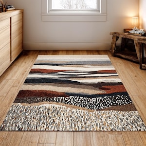 May include: A rectangular area rug with a landscape design. The rug features horizontal bands of color in shades of brown, beige, gray, and black. The bottom section has a textured, speckled pattern. The rug is placed on a wooden floor.