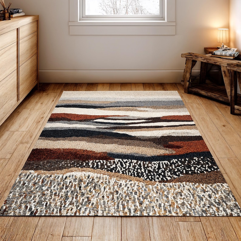 May include: A rectangular area rug with a landscape design. The rug features horizontal bands of color in shades of brown, beige, gray, and black. The bottom section has a textured, speckled pattern. The rug is placed on a wooden floor.