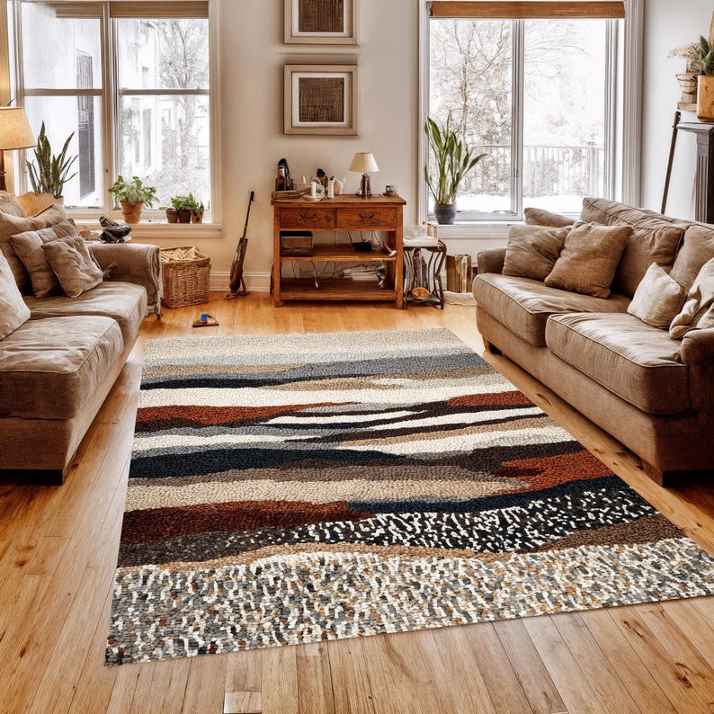 May include: A rectangular area rug with a layered design in shades of brown, gray, and white. The rug features a textured surface and is placed on a hardwood floor in a living room setting. The rug's design resembles a landscape.