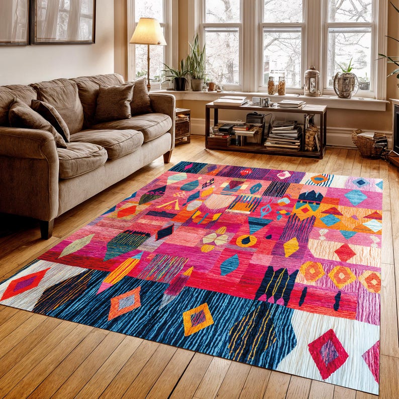 May include: A colourful, geometric area rug with a patchwork design. The rug features pink, red, blue, orange, and yellow. The design includes diamond, rectangle, and abstract shapes. The rug is placed on a wooden floor.